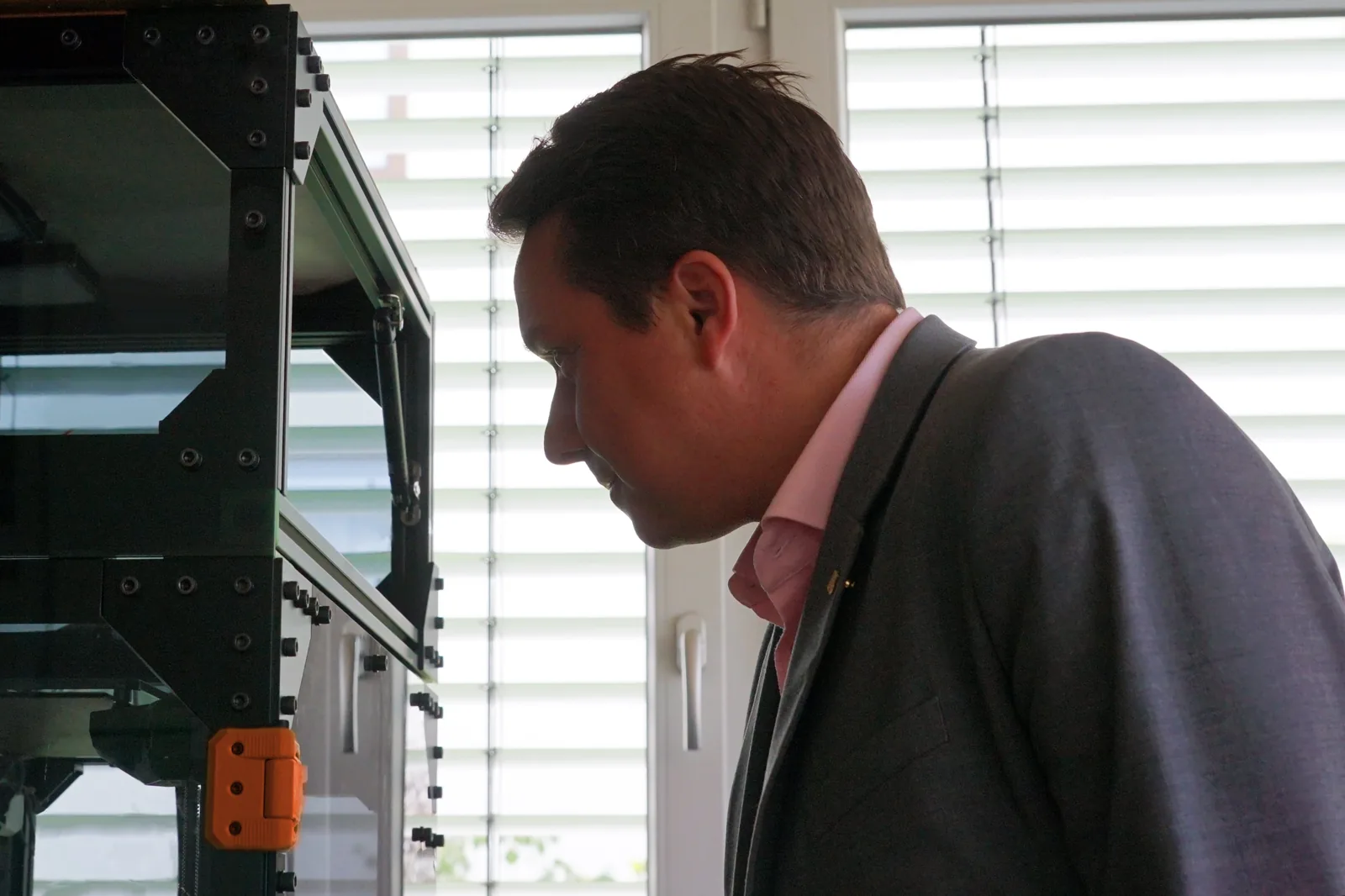 Manuel Hailfinger Landtag Baden Württember CDU in einem Anzug schaut aufmerksam auf ein technisches Gerät in einem Raum mit Jalousien.