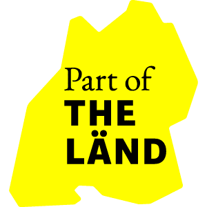 Gelbes Logo mit dem Text 'Part of THE LÄND' in schwarzer Schrift.